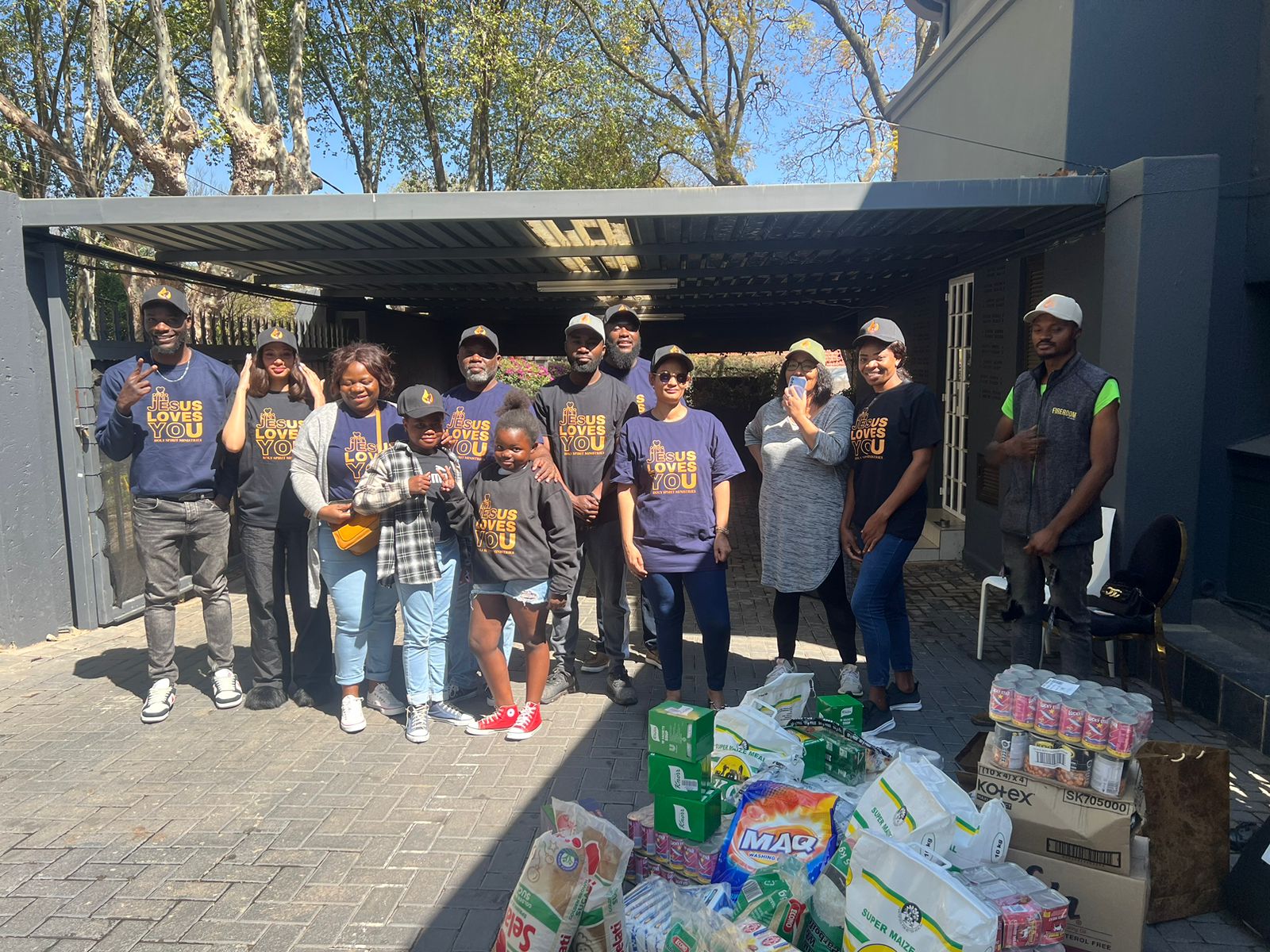 Group of people posing outdoors with boxes and supplies on a paved area.