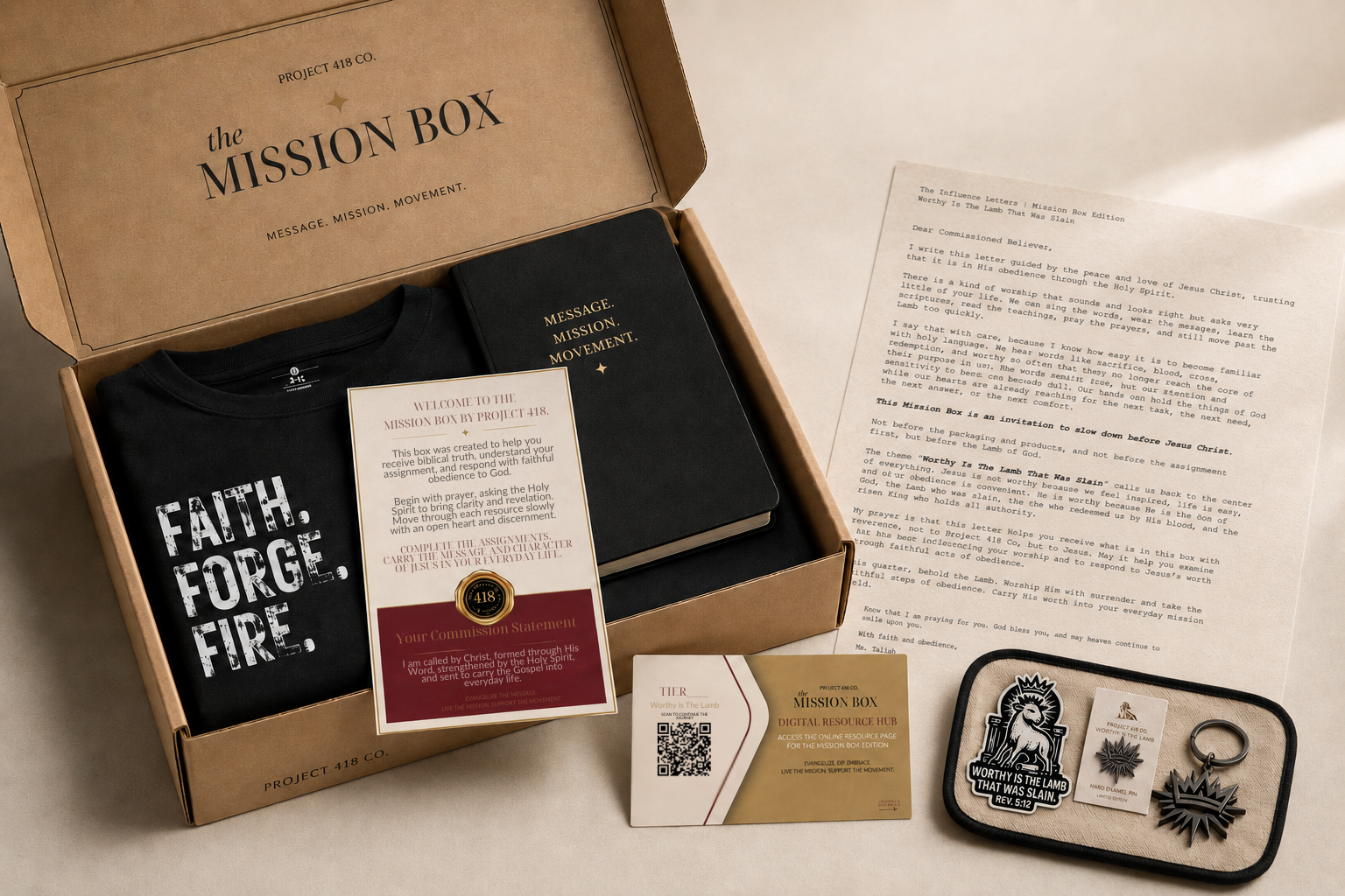 The Mission Box gift set arranged on a light beige surface, including an open kraft cardboard box with a black T-shirt, a black Bible, a welcome letter, a business card, a small tray with pins and a ring, and a printed booklet.
