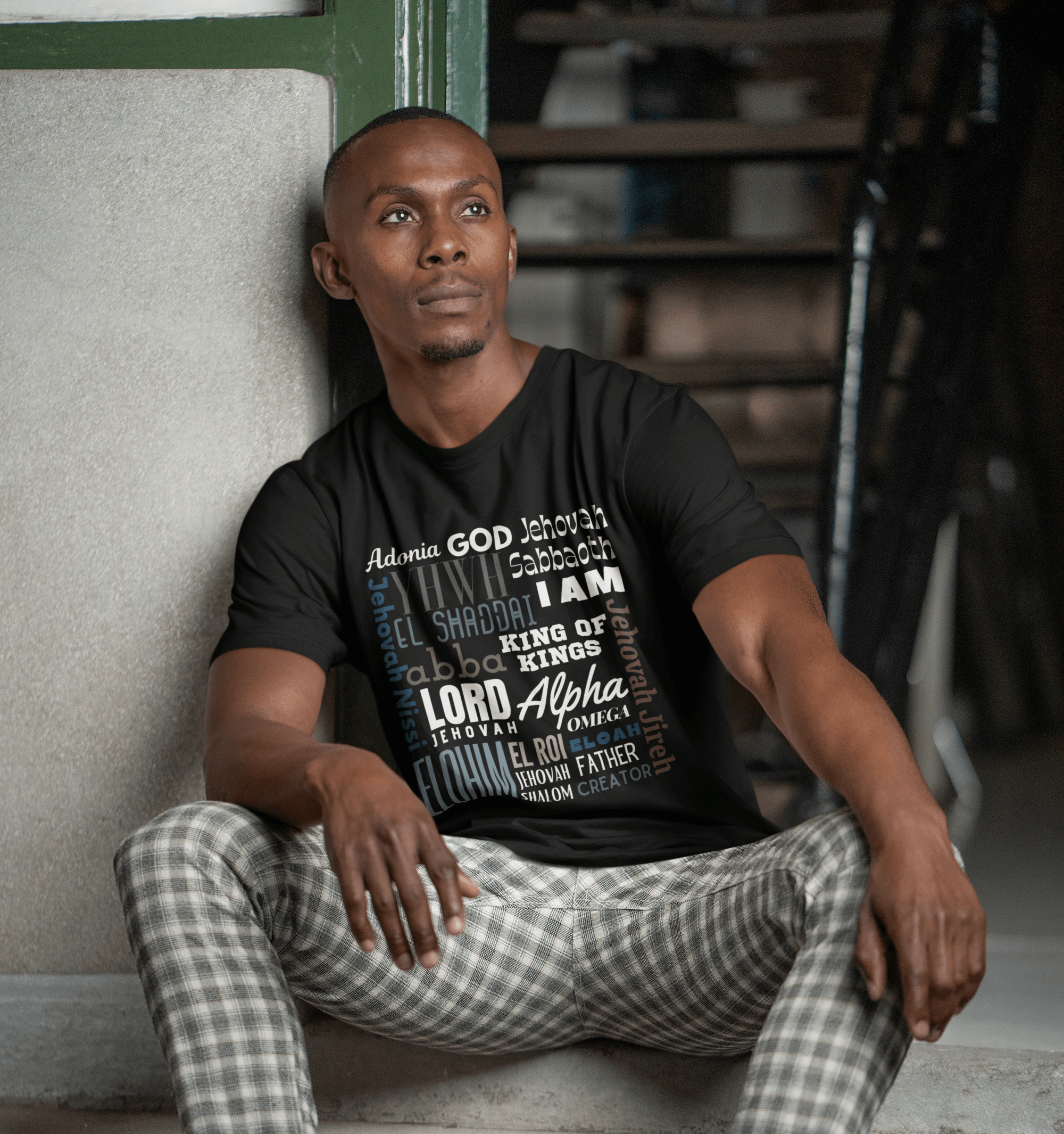 Man sitting on steps wearing a black "God Is" mission t-shirt with text design
