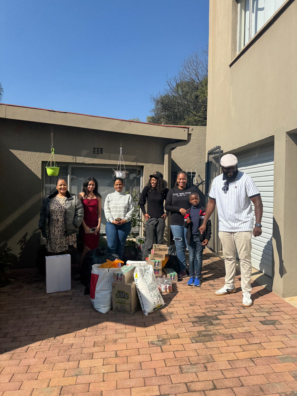 Group of people standing outside a house with boxes and bags on the ground.