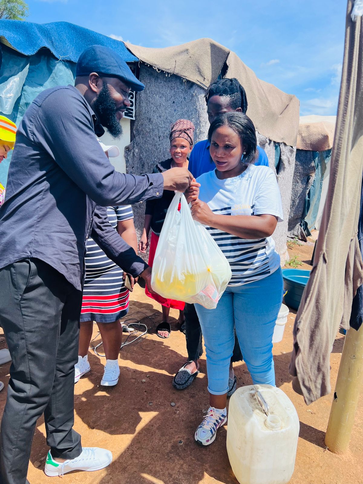 Apostle Randy handing over a bag of food to another person outdoors with a tent in the background